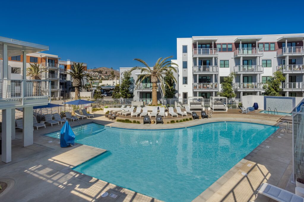 Pool area with shaded chairs, sun tan beds, hot tub, and tropical landscaping