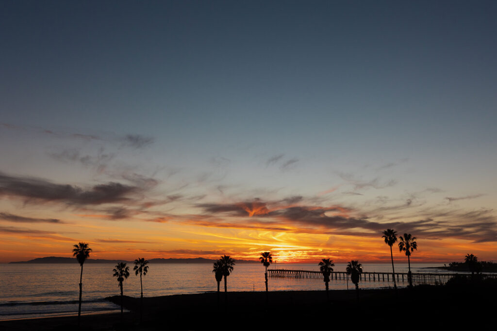 Street side view of sunset at beach with pier and palm trees
