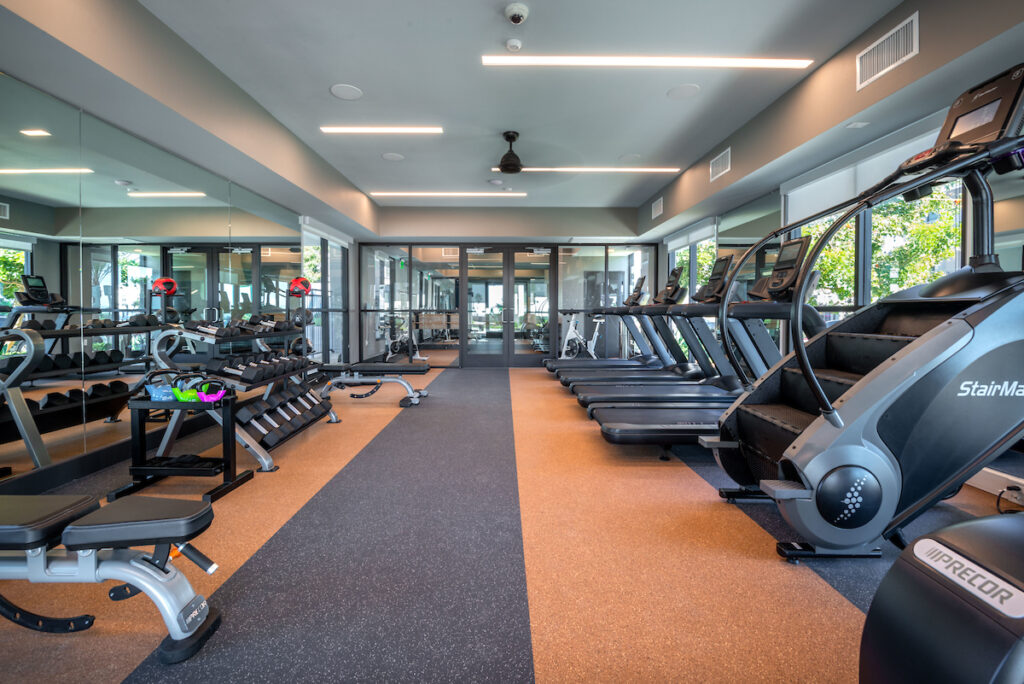 Fitness center with cardio machines including a stair master, treadmills, and Precor ellipticals and strength training equipment including free weights and benches and floor to ceiling mirrors