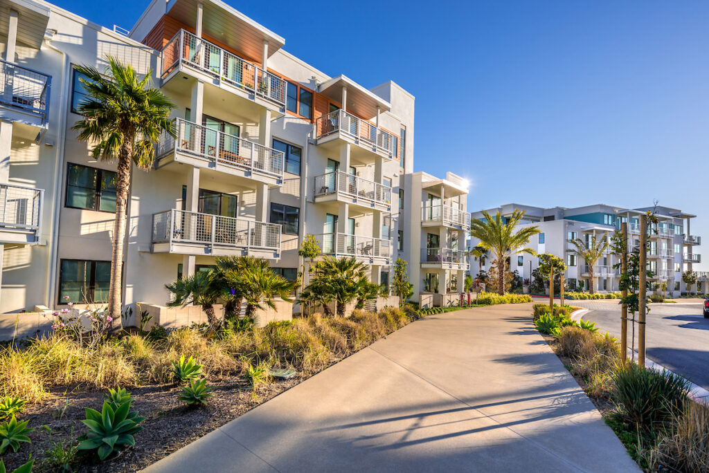 Community apartment building with large balconies and a walkway lined with tropical landscaping