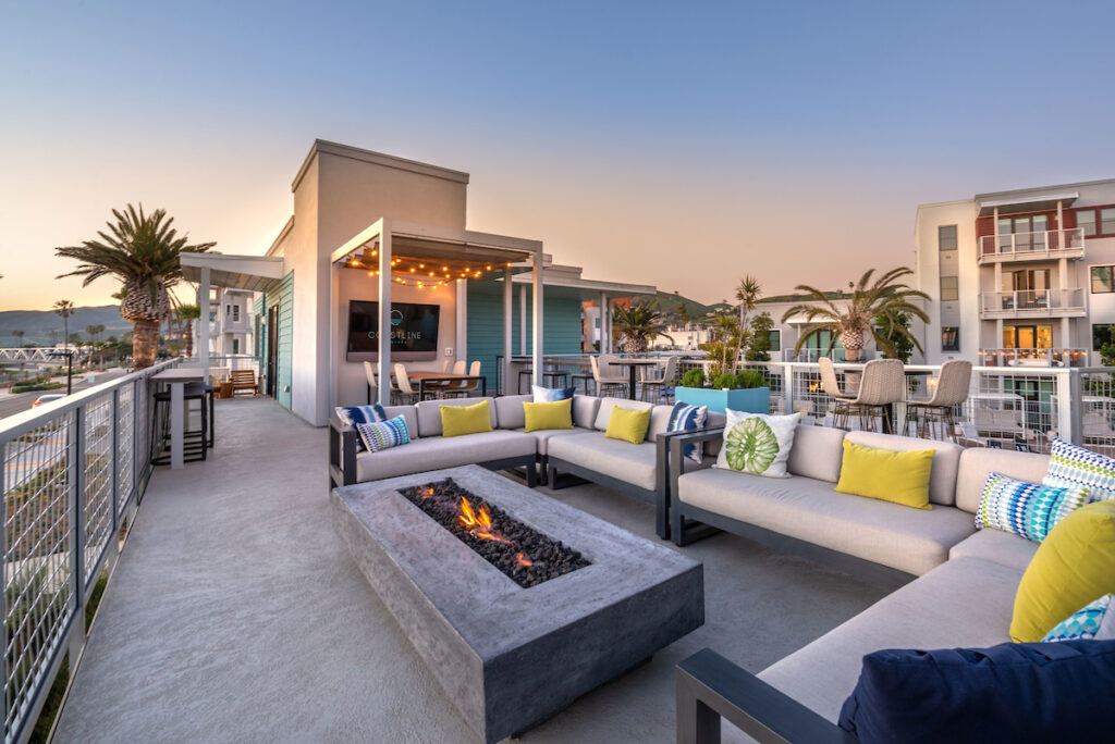 Outdoor sitting area with plush couch seating, fire pit, bistro seating and a flat screen TV, all overlooking ocean views