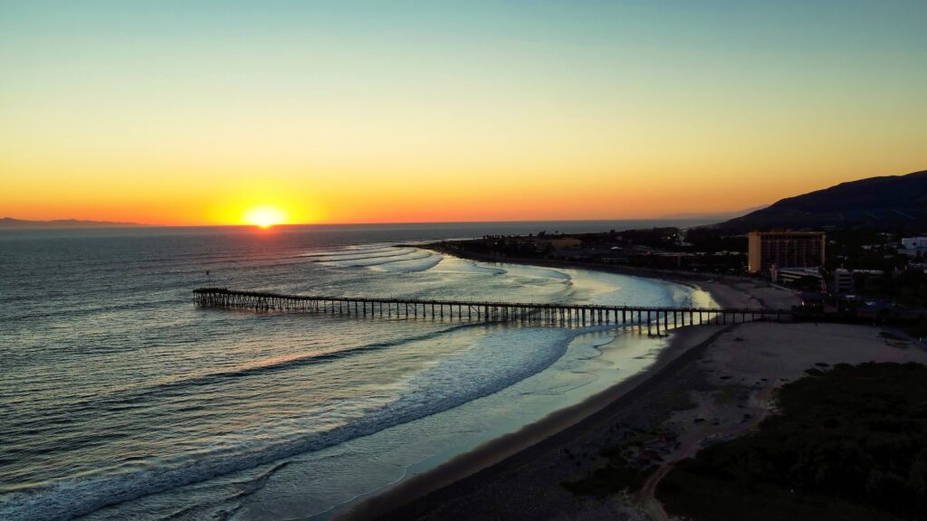 Aerial view overlooking pier, beach, and ocean with sunset